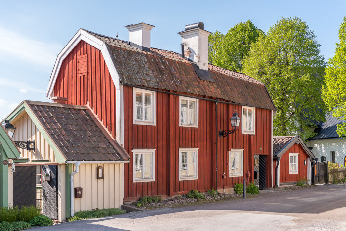 Rött 1700-tals 2-planshus med vita knutar och sammansatt tak i Söderköping, omgivet av grönska.