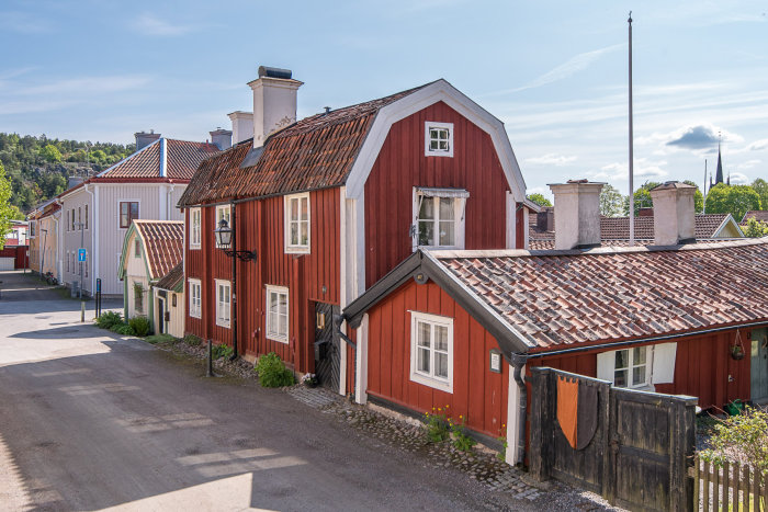 Rödmålat 1700-tals 2-planshus med tegeltak i Söderköping, omgivet av kullersten och andra byggnader.