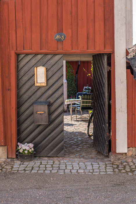 Halvöppen röd träport till 1700-tals hus med inblick mot innergård och cykel.