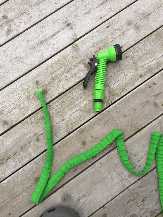 Grön trädgårdsslang med munstycke på trätrall och synliga skador vid olika sektioner.