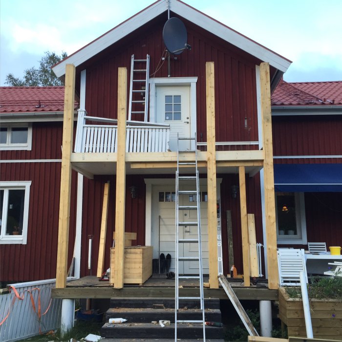 Nyinstallerade träpelare på en farstukvist till ett rött hus med vit dörr och balkong.