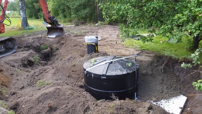 Installation av en svart Ecobox i en grävd grop på en tomt med en grävmaskin i bakgrunden.