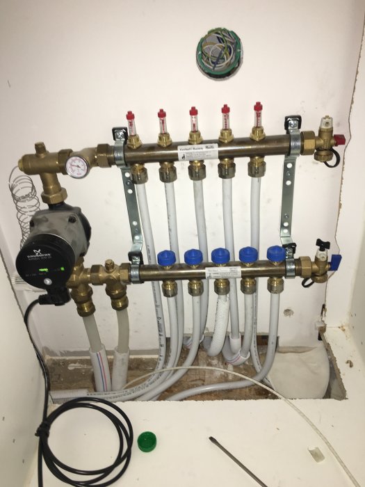 Värmerör och shuntar monterade på vägg, nästan färdigställt värmesystem i byggprojekt.