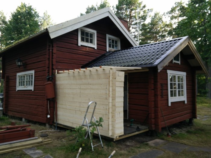 Pågående bygge av en träförlängning på ett rödfärgat hus med svart tak.