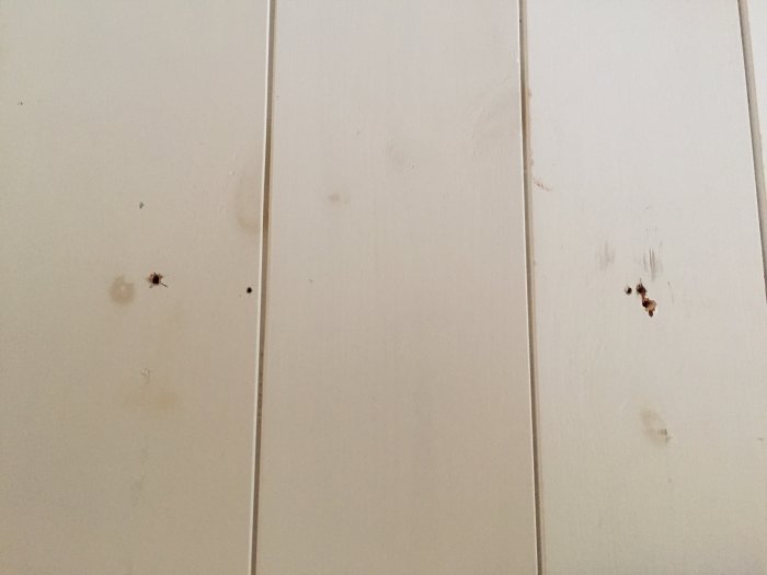 Vit panelvägg med synliga kvistar och flera små hål och skruvmärken.