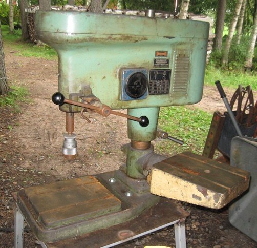 Gammal Valmet pelarborrmaskin med dubbla bord och remdriven Strömberg tvåhastighetsmotor, placerad på en svetsad bock utomhus.