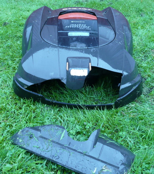 Robotic lawn mower with damaged and detached front bumper on grass.