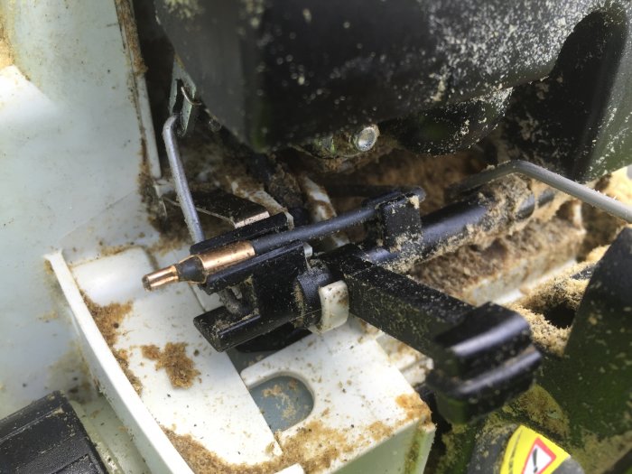 Närbild på en motorsågs reglage med fokus på en lös sladd och kontaktyta, smuts och spån syns runt komponenterna.