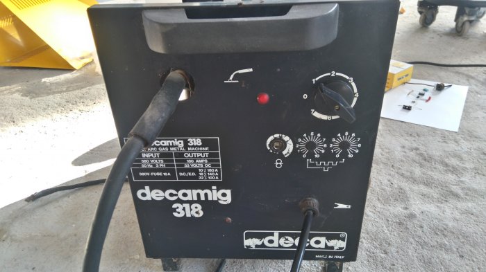Gammal svetsapparat Decamig 318 med kontroller och sladdar, komponenter ligger på golvet i bakgrunden.