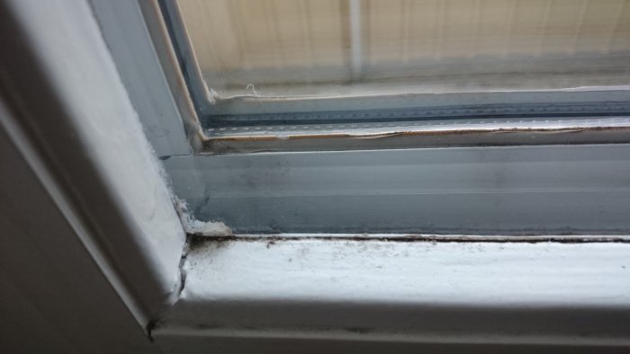Närbild på gammalt fönster med skador och aluminiumtillbyggnad som behöver renoveras.