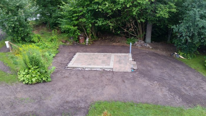 Nygrundlagd friggebodgrund omgiven av nyjord och växtlighet i en trädgård.