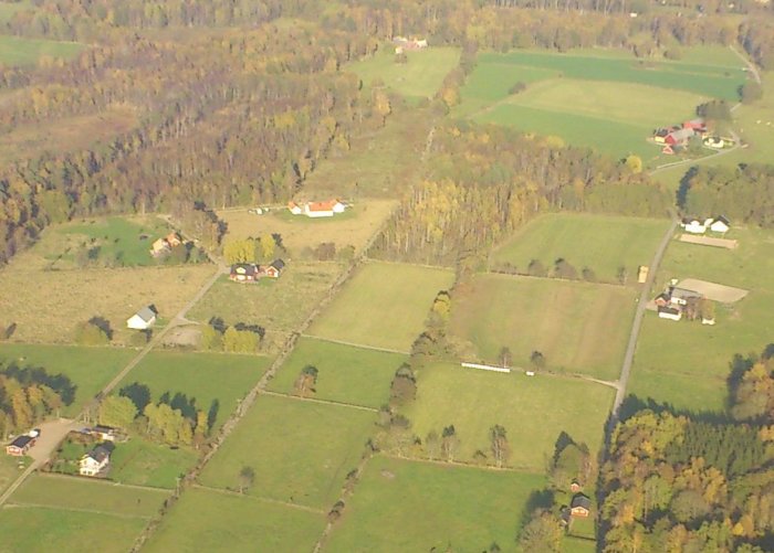 Flygfoto över ett lantligt landskap med fält, träd och flera hus.