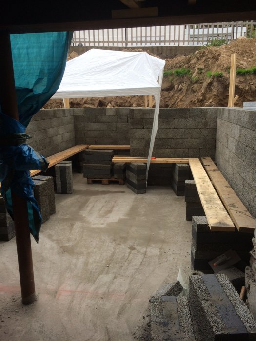 Grundplattan för ett hus och första lagret av betongblock för väggarna, armeringsjärn, och byggmaterial.