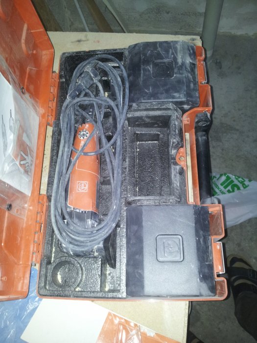 Öppen verktygslåda med oorganiserat arrangerade elektriska verktyg och sladdar.