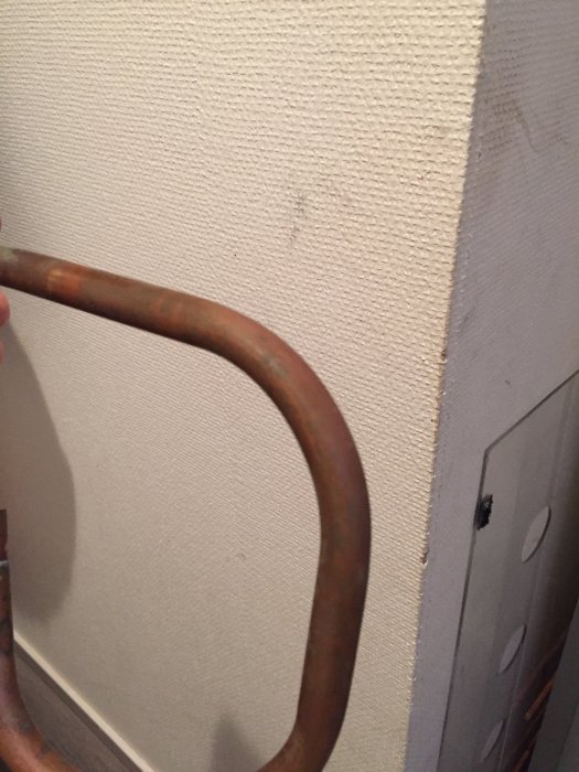 Gammalt böjt kopparör framför en ljus vägg, svårt att fånga exakta detaljer på bild.