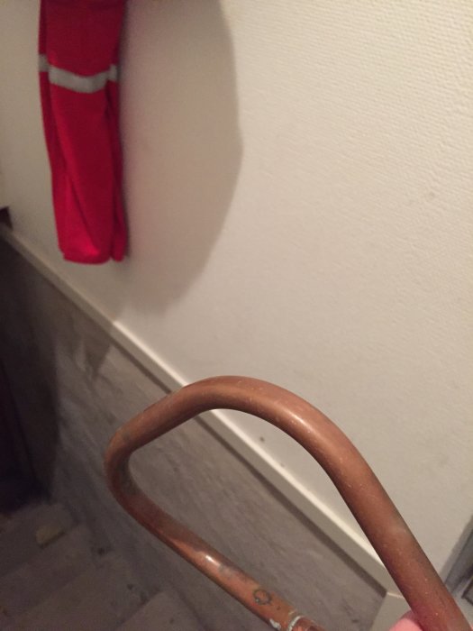 Del av en stege med en röd trasa som hänger på en krok mot en vit vägg.
