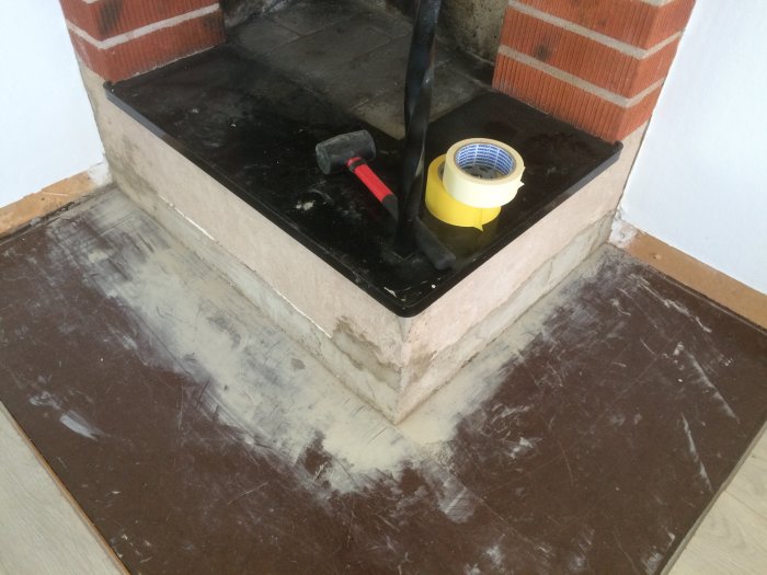 Ett hörn av ett rum under renovering med putsade ytor, en hammar och tejp på golvet.
