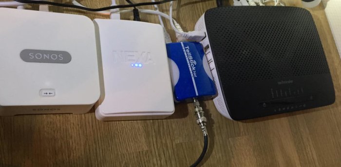 En Sonos Bridge, Nexa bridge och Tellstick Net bredvid en router på ett bord.