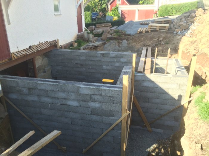 Källare under konstruktion med Leca-block väggar stöttade av trästockar, redo för putsning.