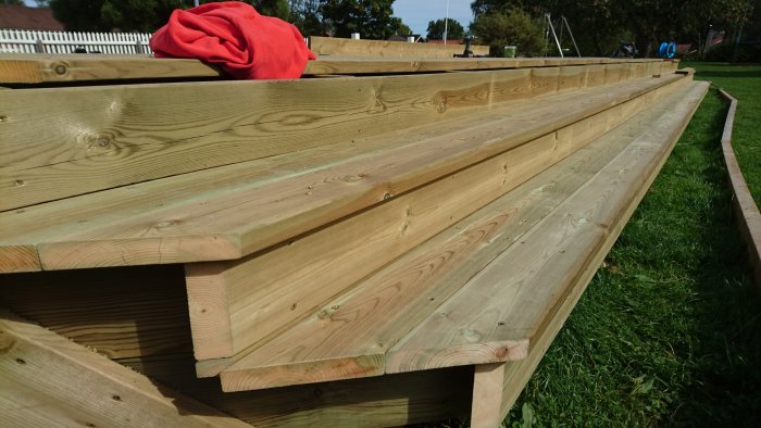 Nybyggd trätrappa utomhus med flera rader av trall, röd tröja på ett steg.