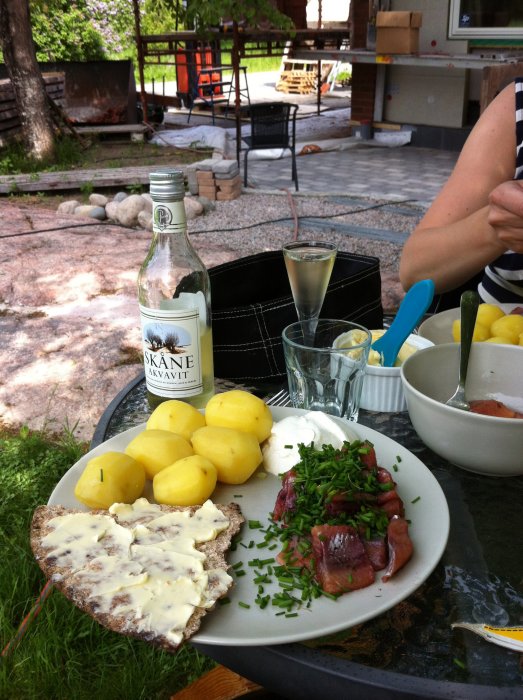 Lunch med potatis, sill, knäckebröd och Skåne Akvavit framför byggprojekt med murarblandare och material.