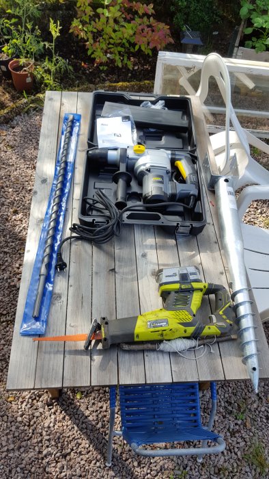 Borrhammare, långt betongborr och jordankare på ett träbord, redo för användning i stenig mark.
