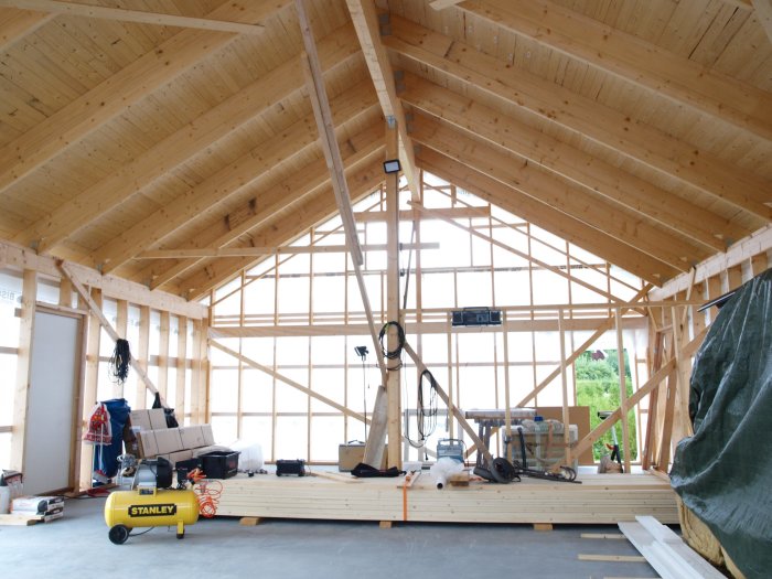 Nybyggt trähus med öppen stomme, nylagd och slät betongplatta och byggmaterial på golvet.