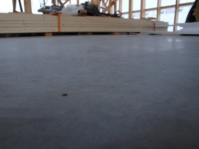 Nyslagen betongplatta på byggprojekt med synliga träplankor i bakgrunden.