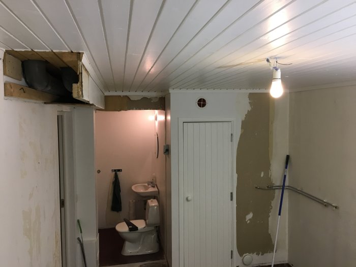 Pågående badrumsrenovering med öppet takutrymme, delvis avtäckt vägg och installerad toalett.