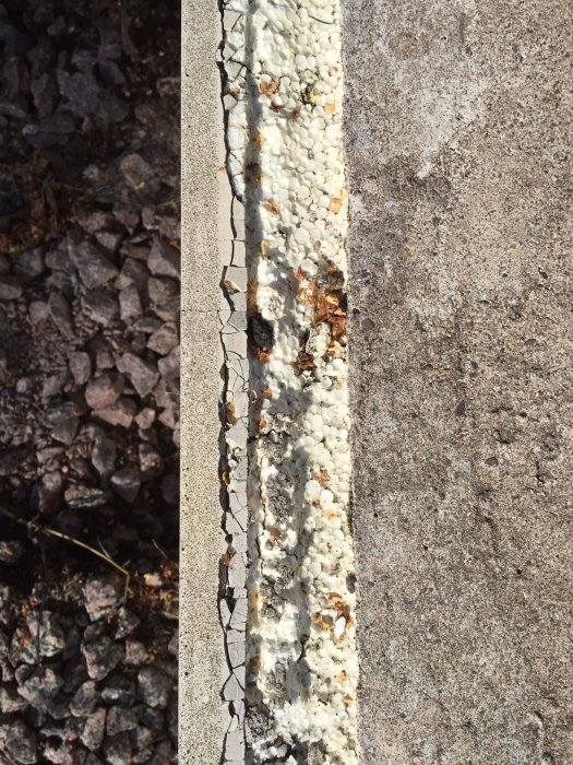 Betongplatta med skadade kanter som exponerar underliggande frigolitisolering mot grusmark.