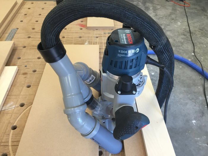 Överhandsfräs monterad med dammuppsamlingsrör redo att fräsa fingergrepp i MDF-fronter på arbetsbänk.
