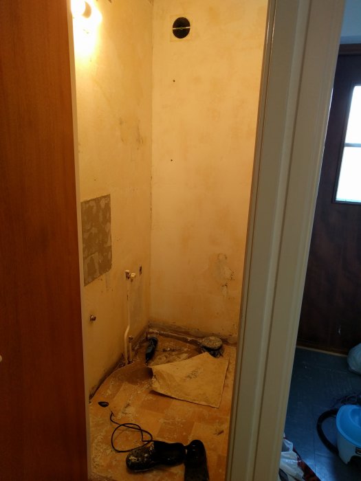 Rum under renovering med borttagen tapet och synligt doslock högt upp på väggen samt renoveringsverktyg och skräp på golvet.