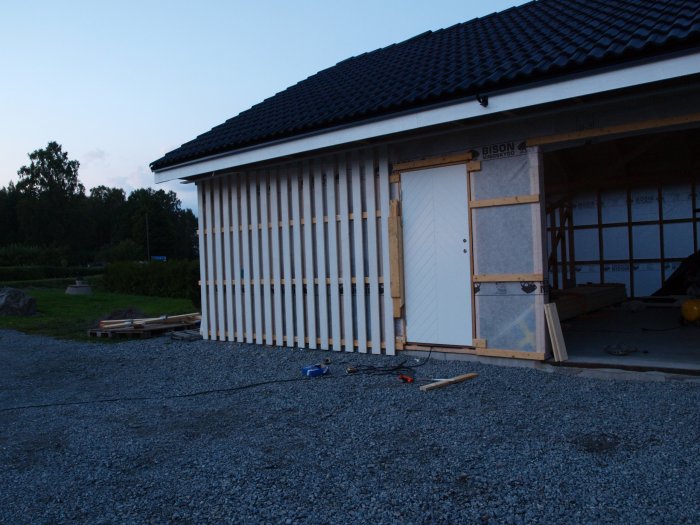 Delvis uppbyggt garage med nygrundade panelbrädor och byggmaterial på marken.