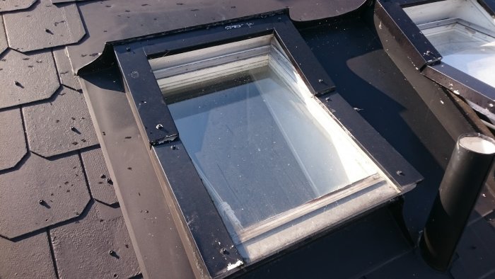 Takfönster på ett radhus med flagnande färg och synlig plåtkonstruktion runtom.