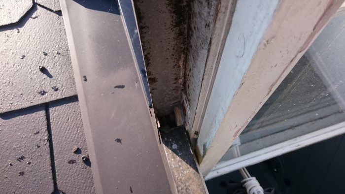 Närbild på ett gammalt takfönster med flagnad färg och synliga tecken på slitage, med taktegel i förgrunden.