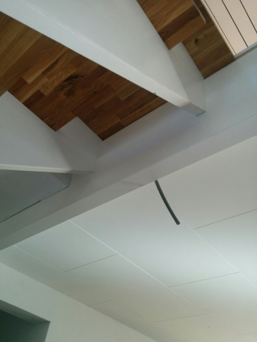 Hvitt tak med åpne bjelker av tre. En kabel stikker ut mellom paneler.