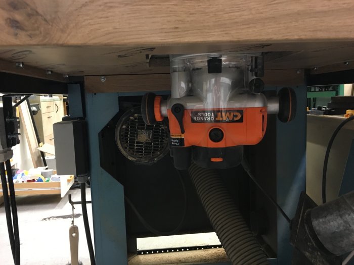 Orangefärgad fräsmaskin monterad under en arbetsbänk i en verkstad.