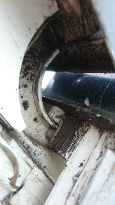 Närbild på gammalt fönsterhörn med flagnande färg och detalj av gångjärn.