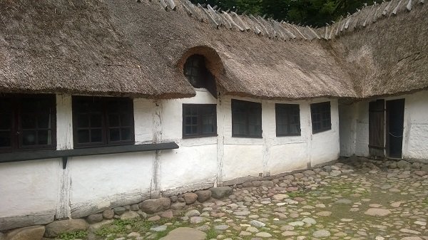 Traditionellt hus med stråtak, vitkalkade väggar och små fönster, stående på en stengrund.