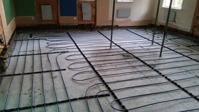 Installation av golvvärme med slingor på betonggolv och ett golvvärmeskåp på väggen.