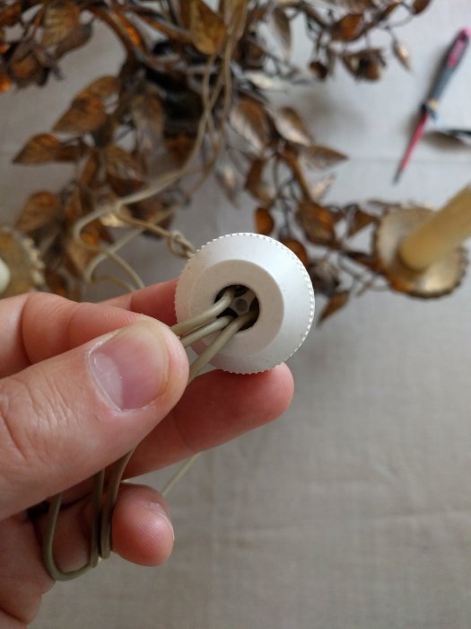 Hand håller en elektrisk lampsockel med tre synliga trådar och delvis suddig bakgrund.
