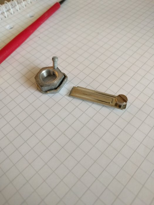 Metallisk kronmutter och platt jordningsklämma på rutat papper, elrenoveringsdetaljer.