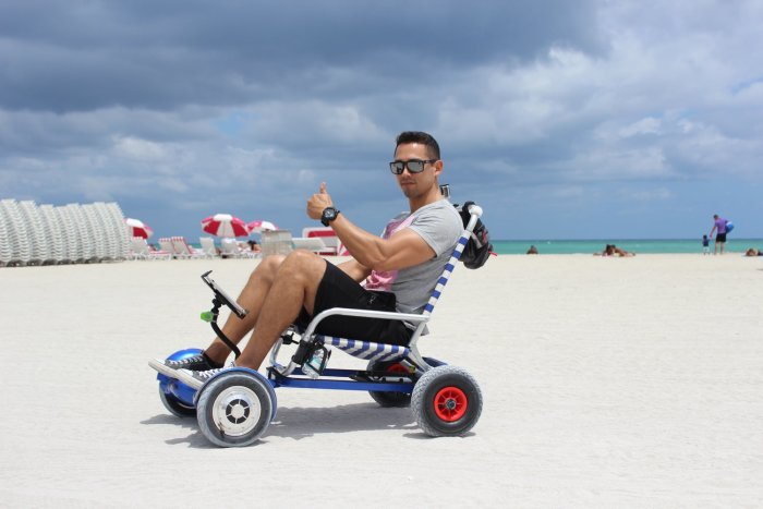 Man på stranden ger tummen upp medan han sitter i en hoverboard-gokart med hjul och styrreglage.