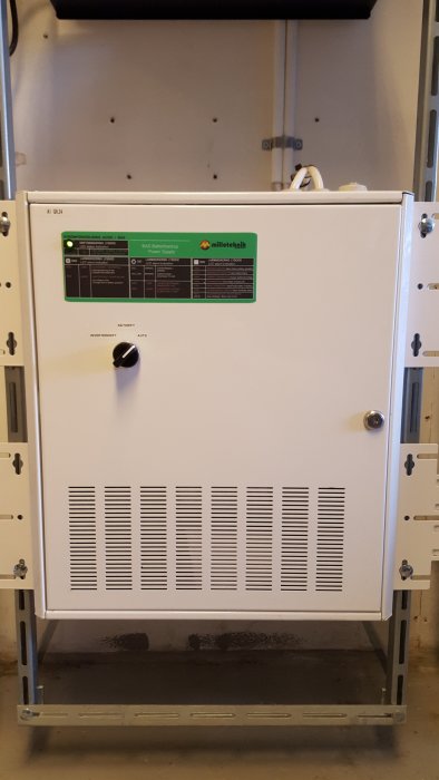 Vit skåplucka med ventilationsgaller, etiketter, rattar, monterad på en ställning, troligtvis teknisk utrustning.