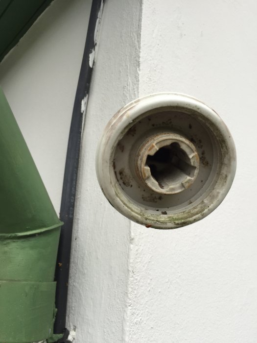 Delvis demonterad fastsatt hållare på vit vägg vid sidan av grönt fönsterfoder.