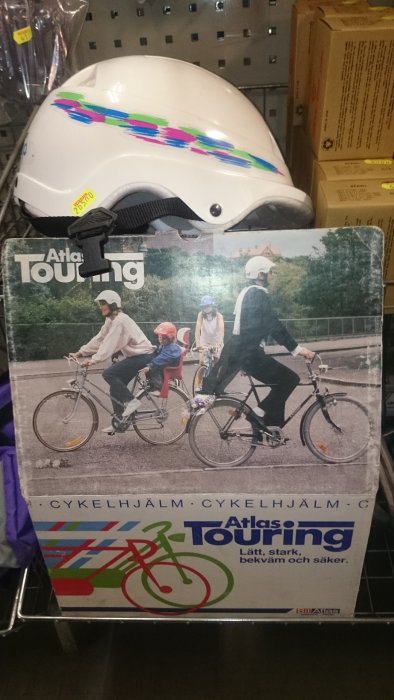 Retro vit cykelhjälm med färgglada streck på kartong med bild av cyklister, Atlas Touring.