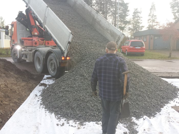 Lastbil tippandes grus i en hög med en person i förgrunden som håller i en spade.