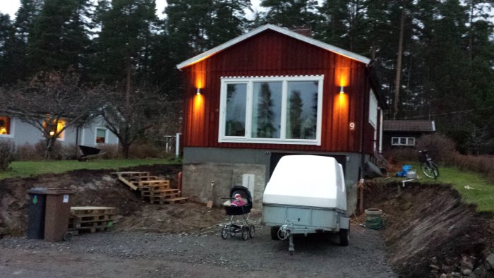 Nyligen grävt område framför hus med grusgång, släpvagn och barnvagn parkerad utanför.