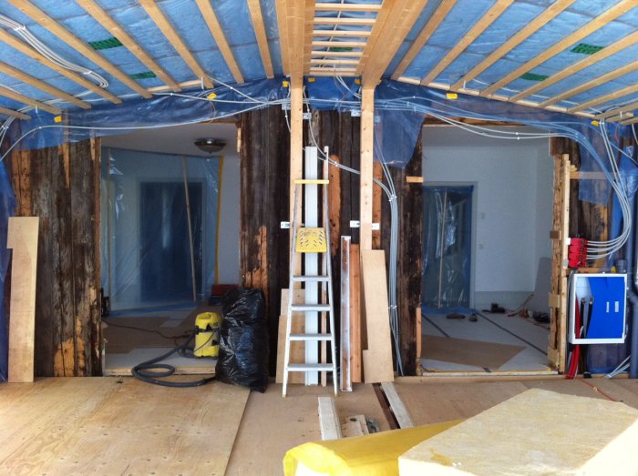 Interiör av en renovering med öppningar i stående timmervägg, byggmaterial och en stege.