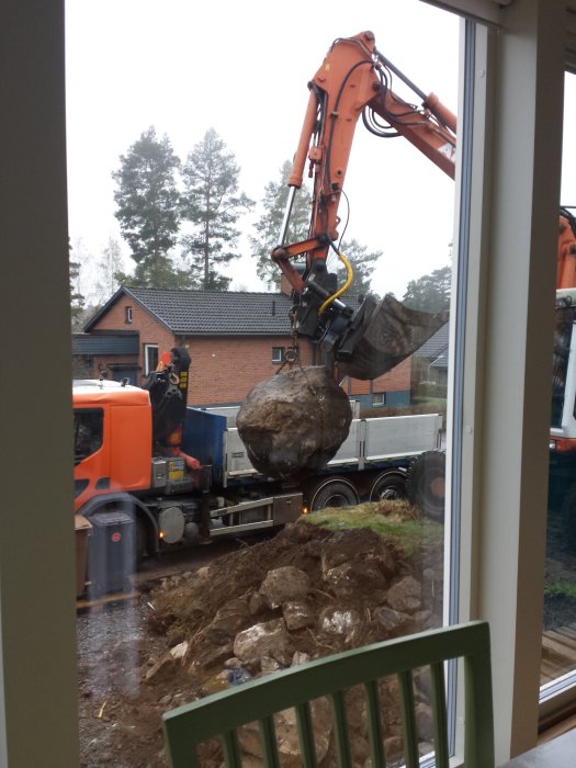 Grävmaskin lyfter stor sten medan lastbil och sprängd berggrund syns vid dräneringsprojekt.